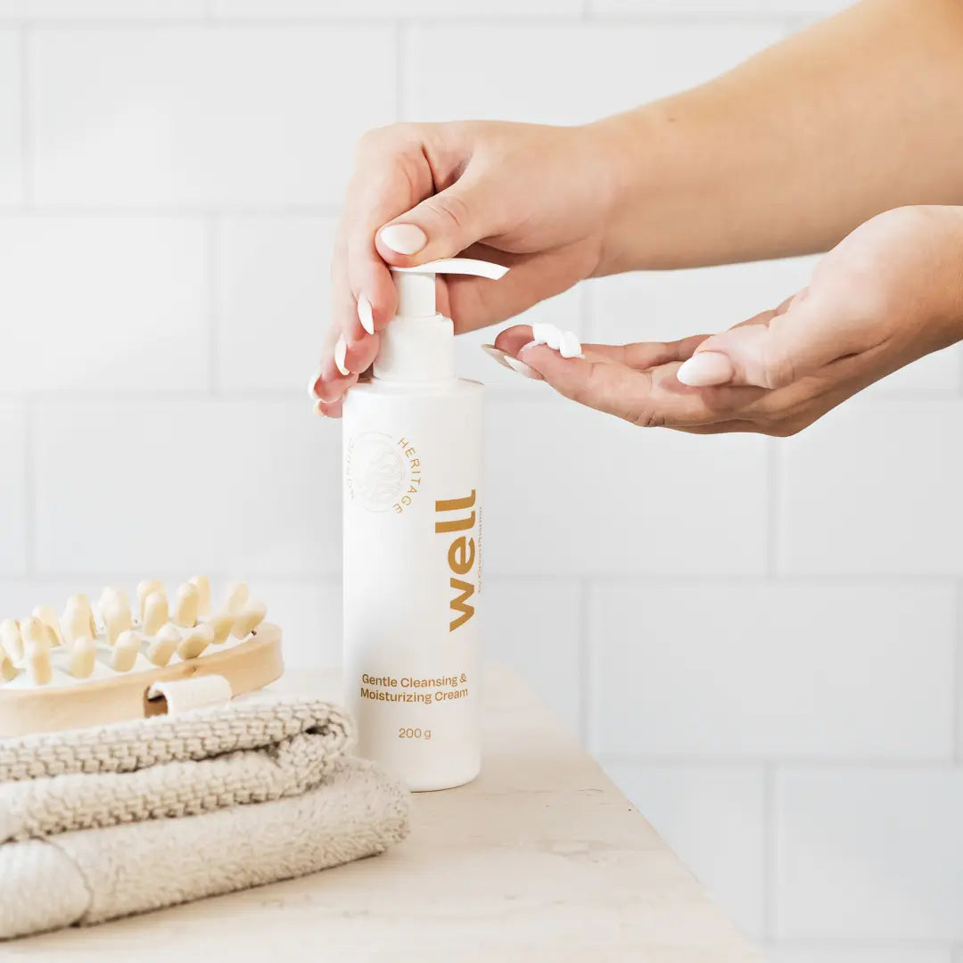 Person applying cream from Well by Orion Pharma branded bottle on a bathroom shelf with towels and a brush.