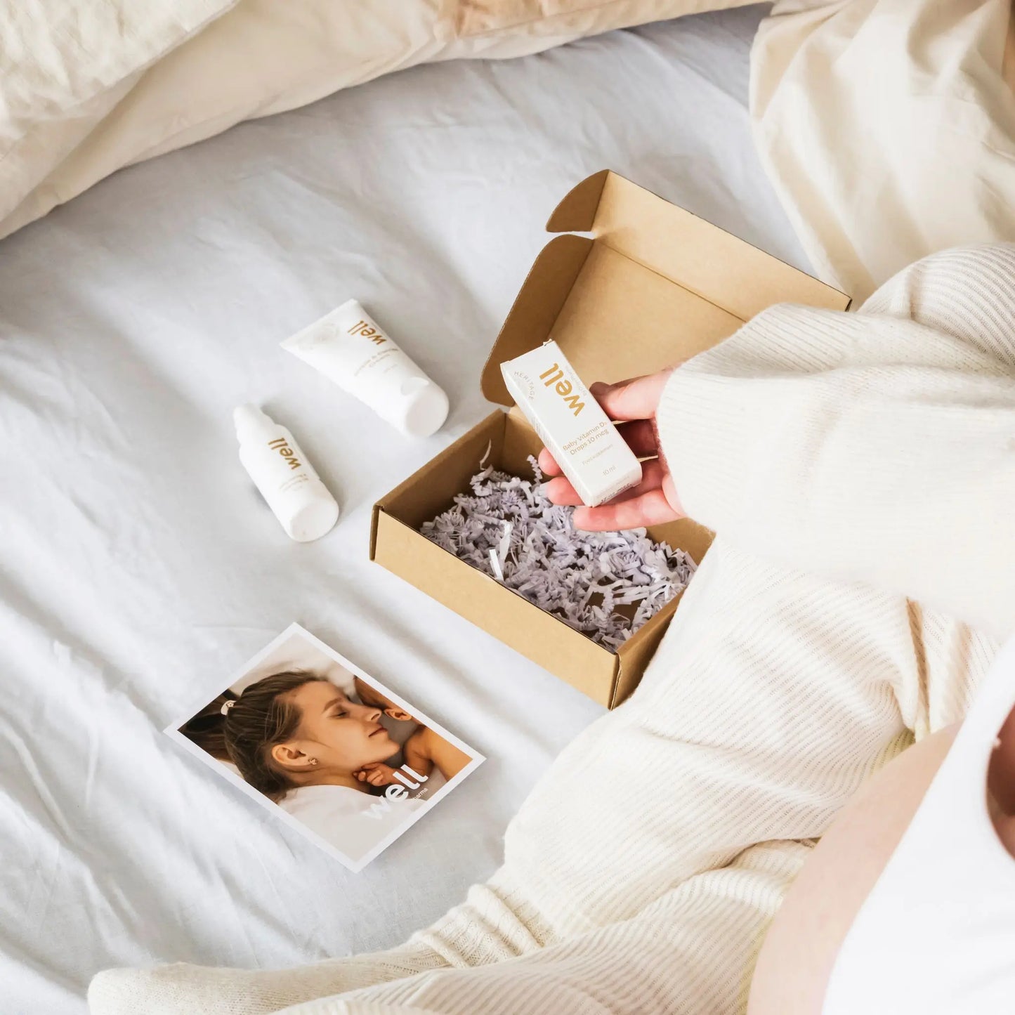 Person holding a Well by Orion Pharma skincare product next to an open box on a bed