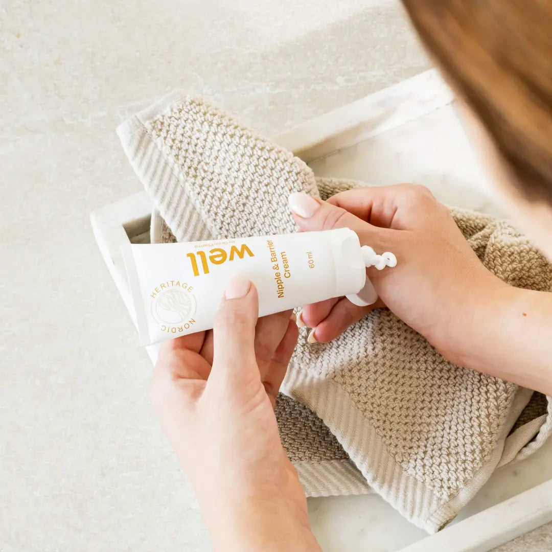 Person applying a tube of cream labeled Well by Orion Pharma to a baby's bottom.