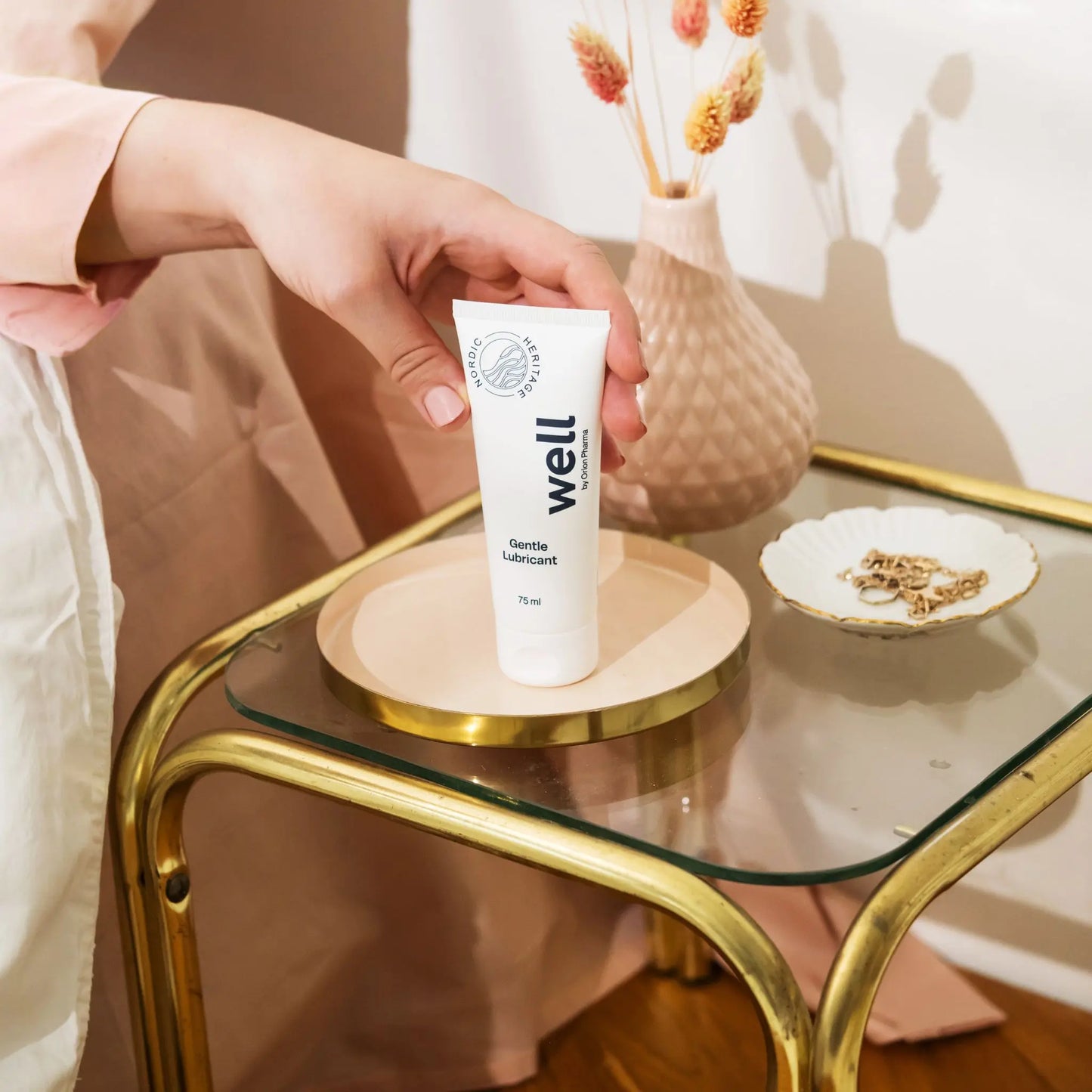 Hand holding a 'well' product on a glass table with decorative items.