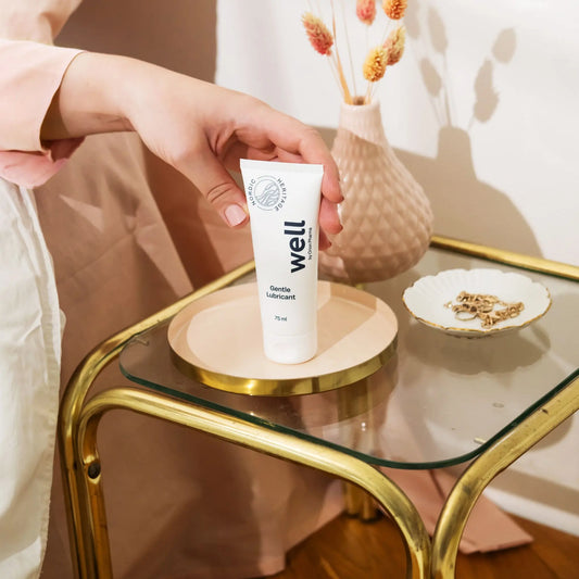 Hand holding a 'well' product on a glass table with decorative items.