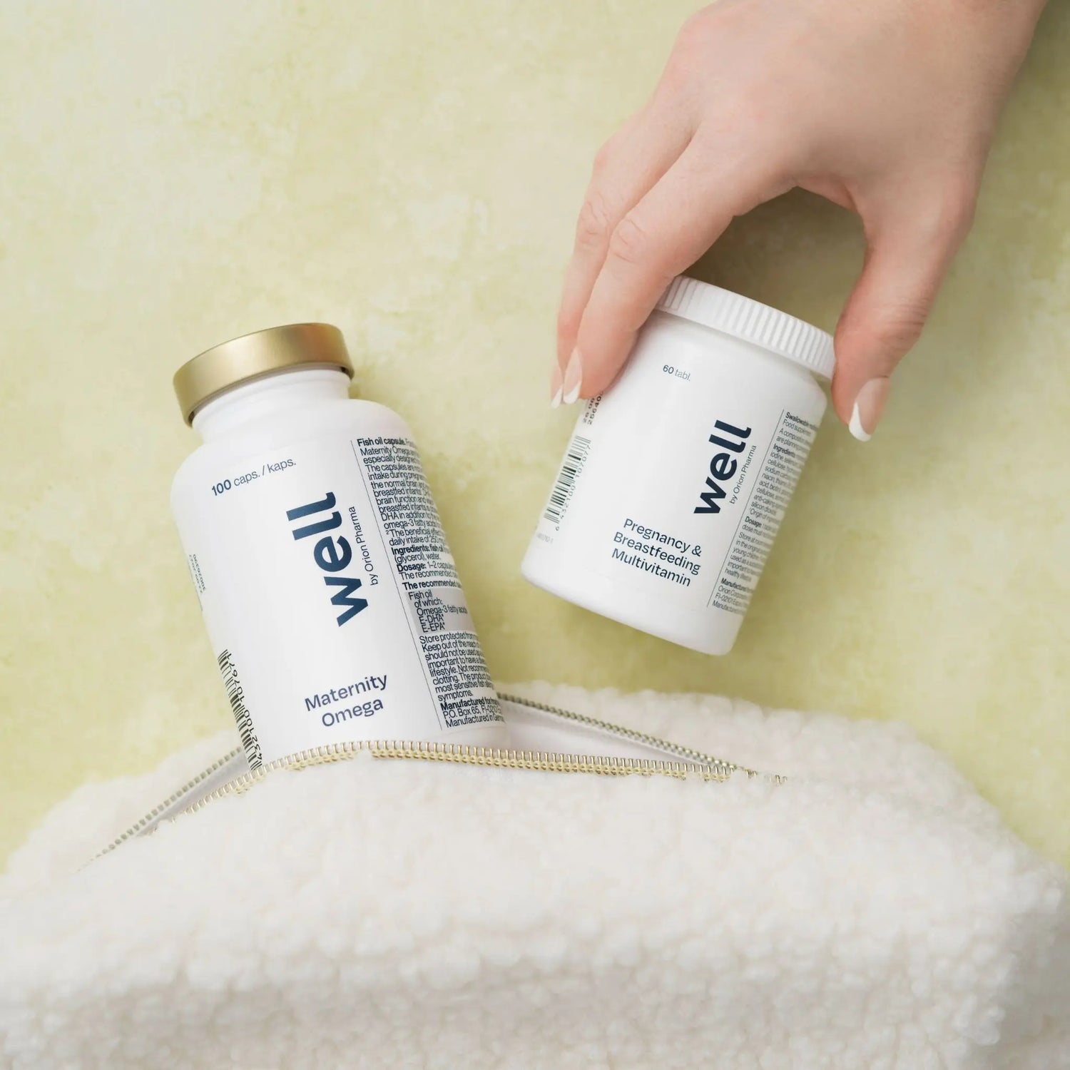 Two 'well' branded supplement bottles on a textured surface with a hand reaching for one bottle.