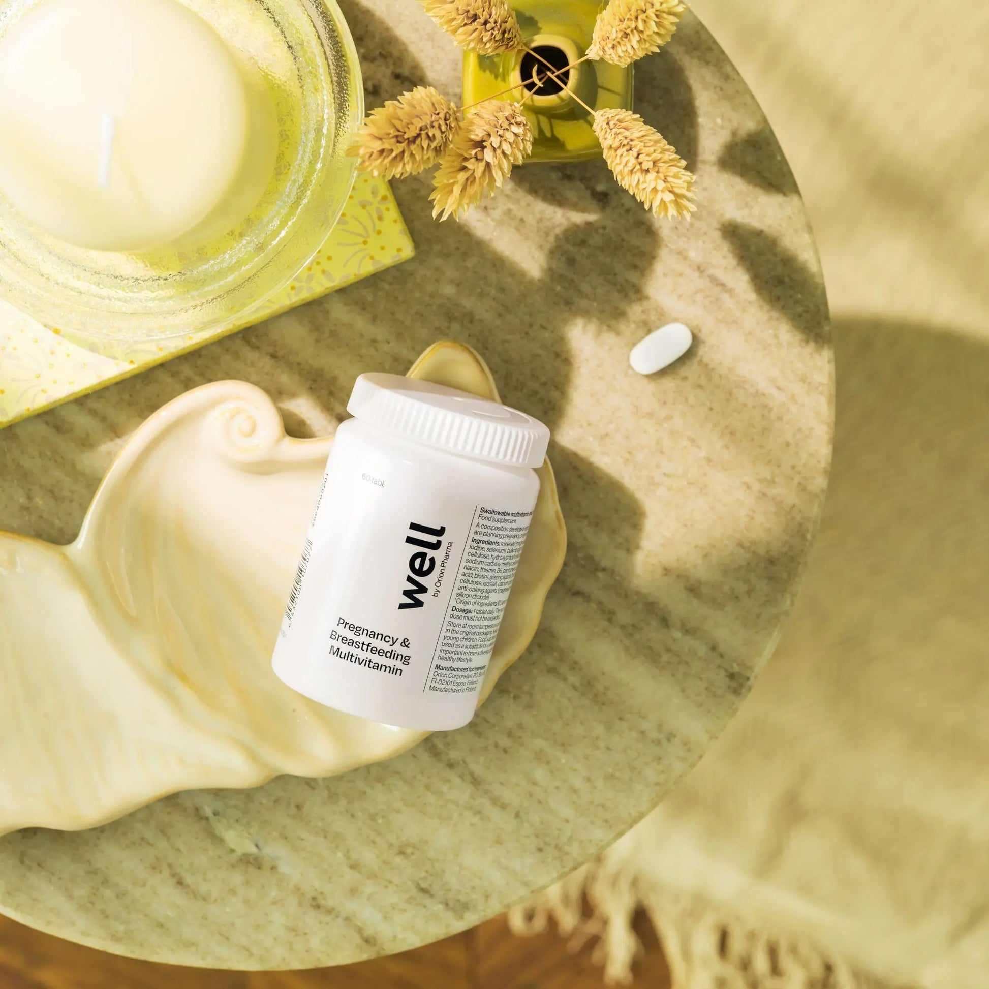 Vitamin bottle labeled 'well' on a wooden surface with a candle and flowers.