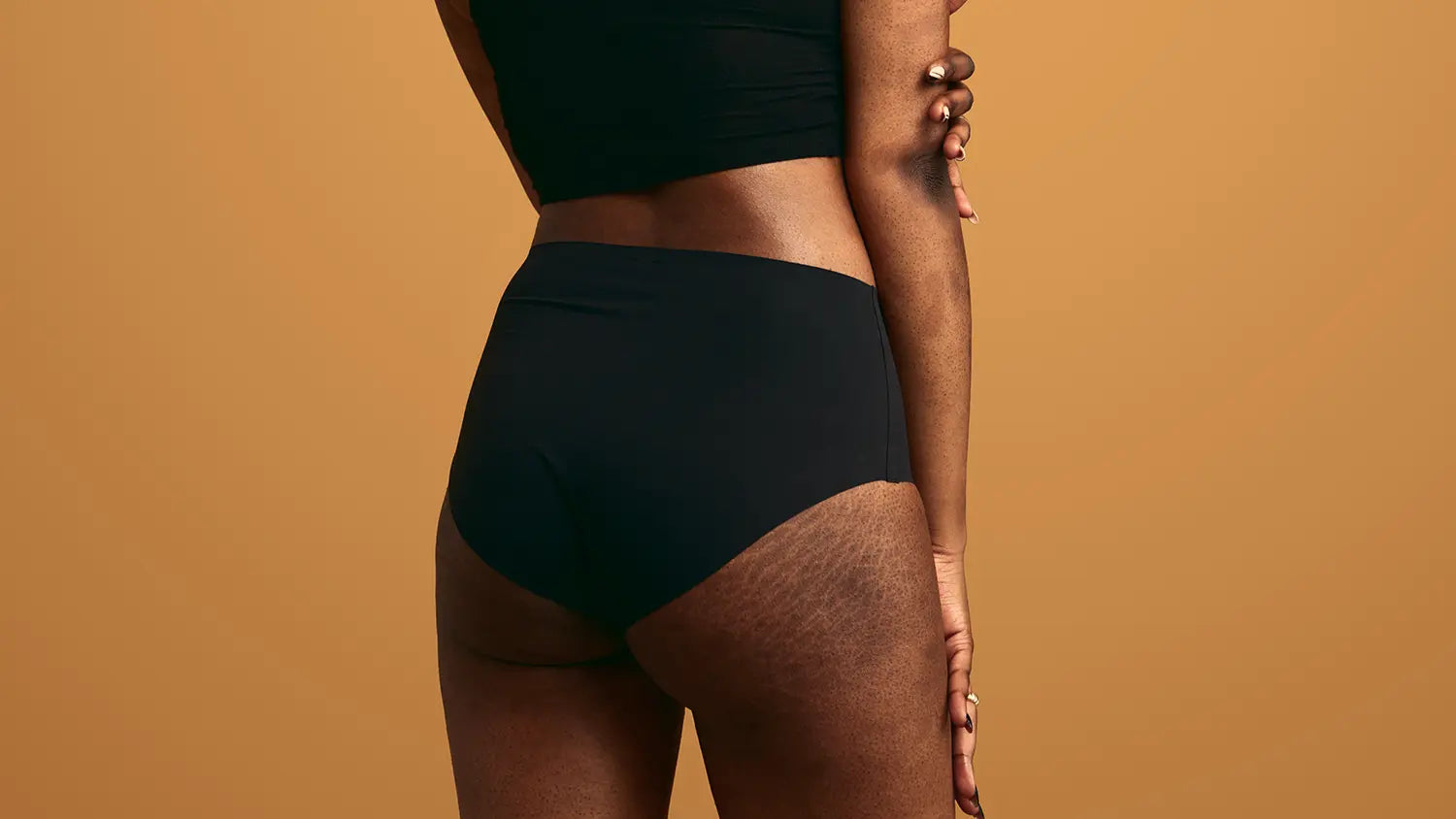 Person wearing black high-waisted underwear against a brown background
