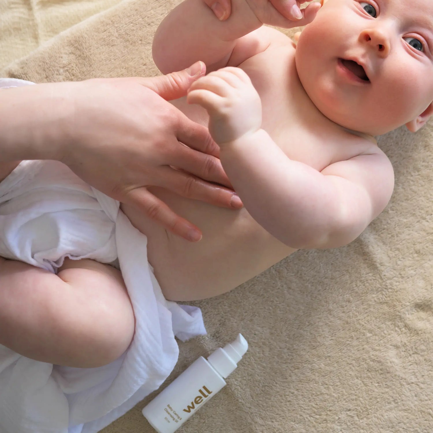 Baby liggande på en handduk med en flaska lotion bredvid sig.