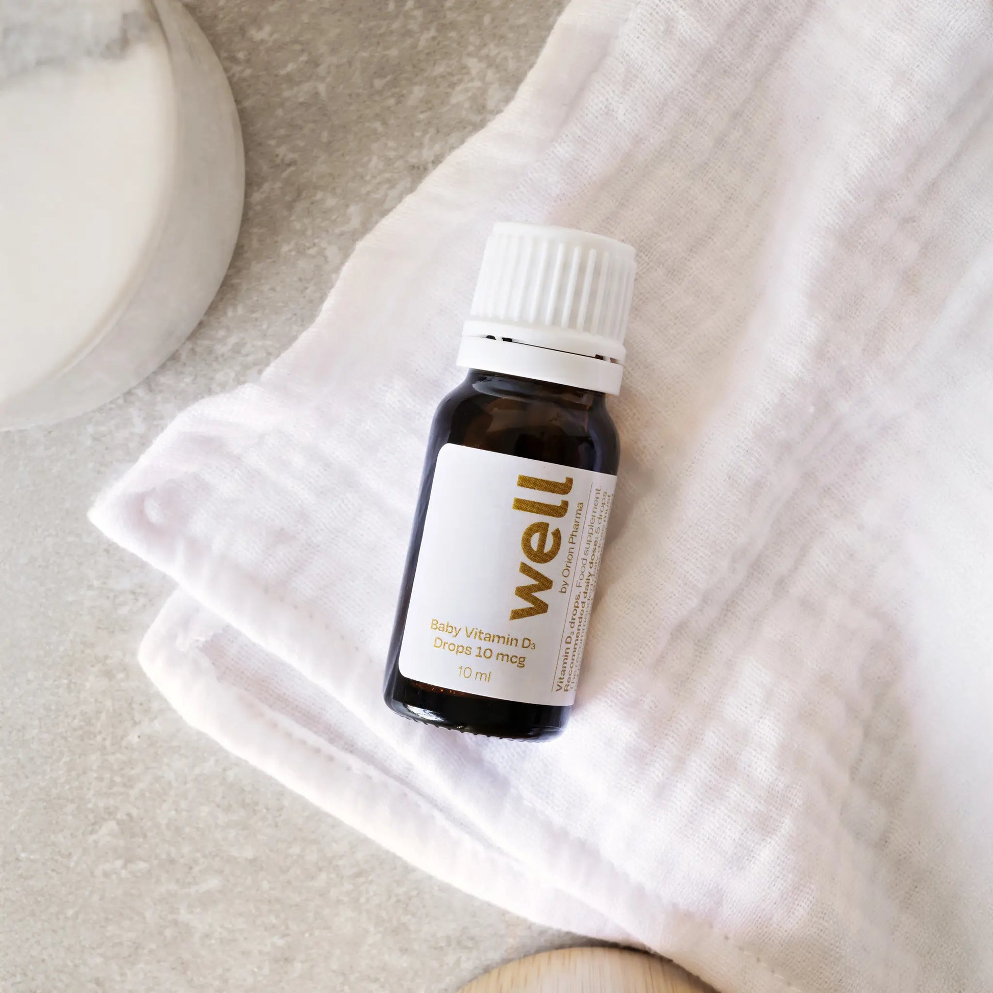 Flaska med Well by Orion Pharma baby vitamin D3-droppar på en vit strukturerad yta.
