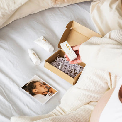 Person holding a Well by Orion Pharma skincare product next to an open box on a bed