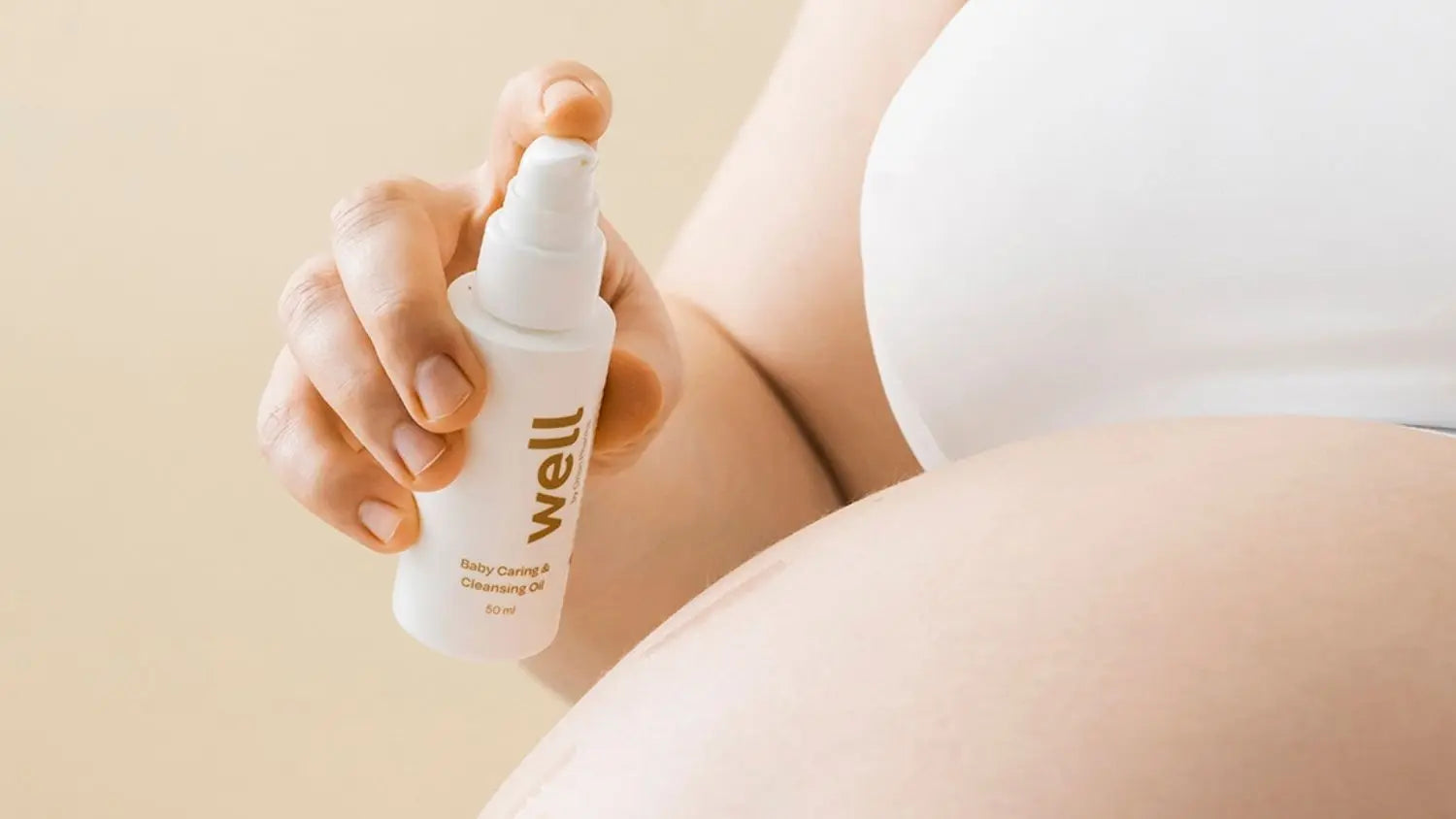 Person holding a bottle of 'well' baby oil on a beige background
