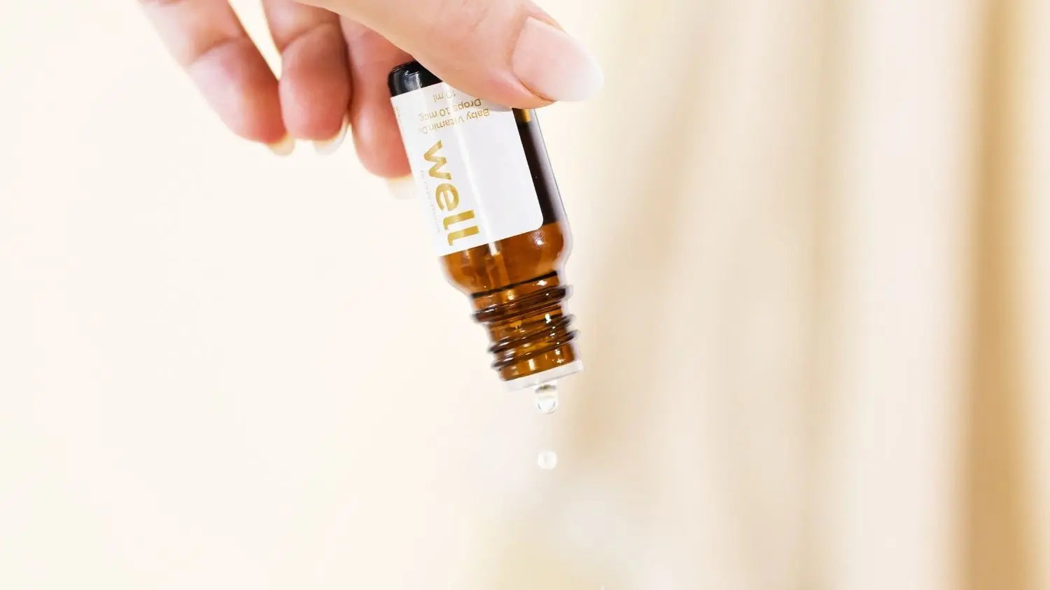 Hand holding a small brown bottle labeled 'well' against a light background