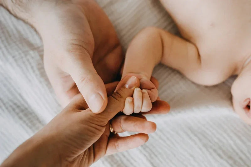 Close-up of adult hands holding a baby's hand on a soft surface