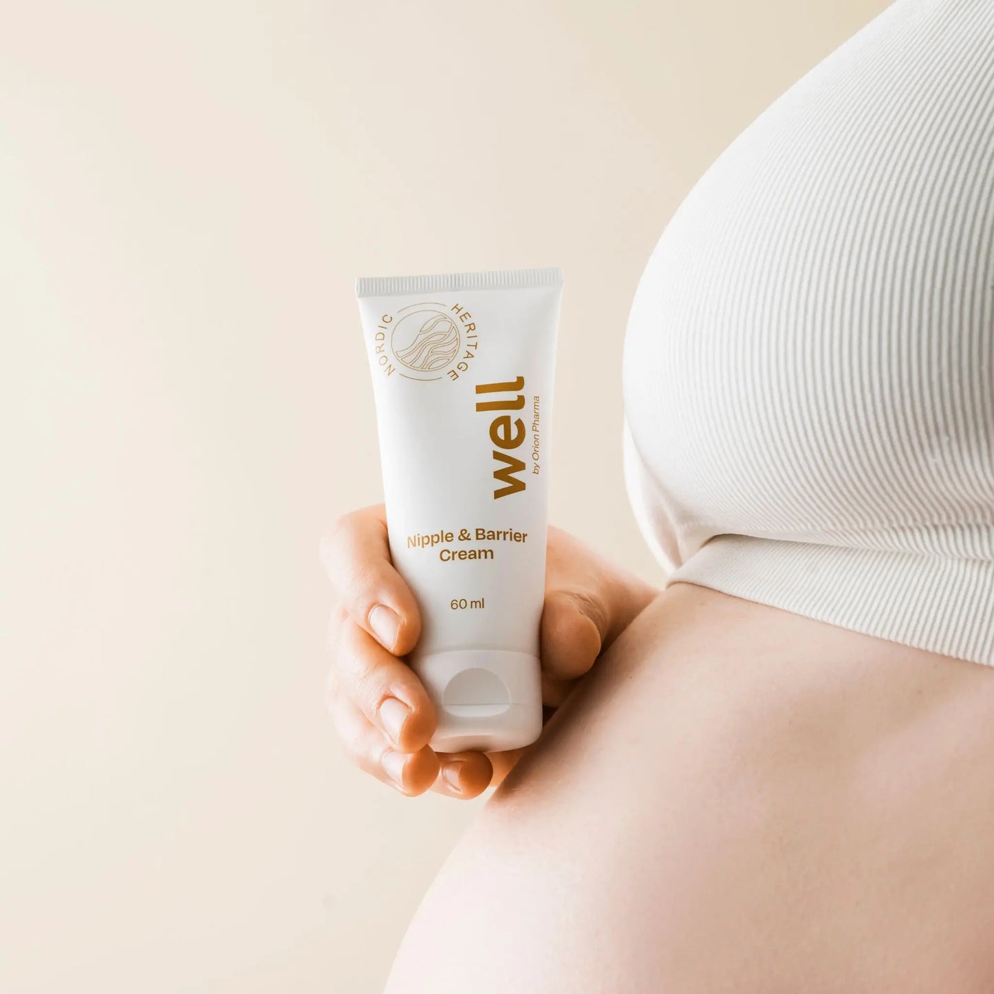 Hand holding a tube of Well by Orion Pharma Nipple & Barrier Cream against a beige background