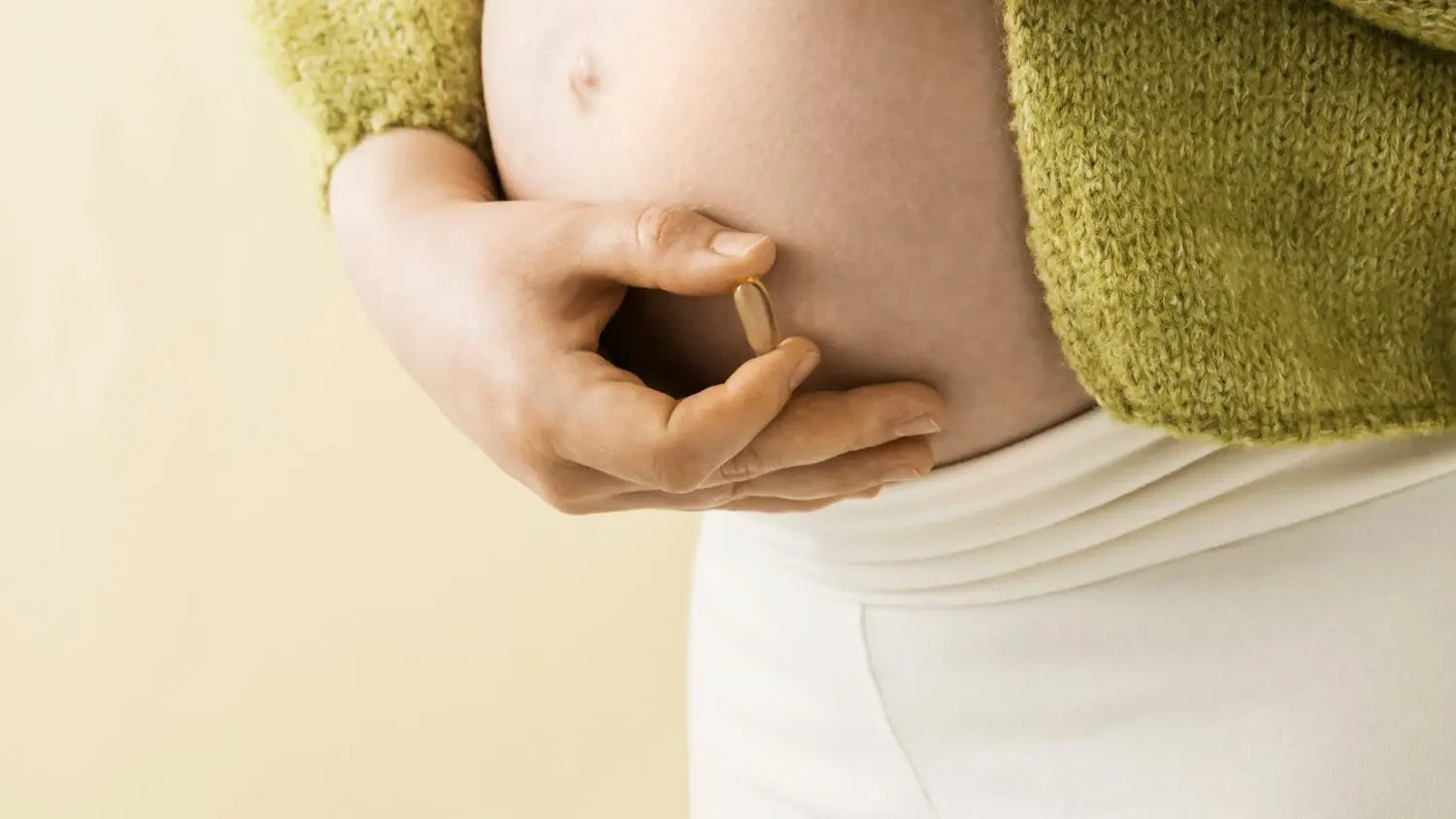 Person wearing a green sweater holding their pregnant belly against a beige background