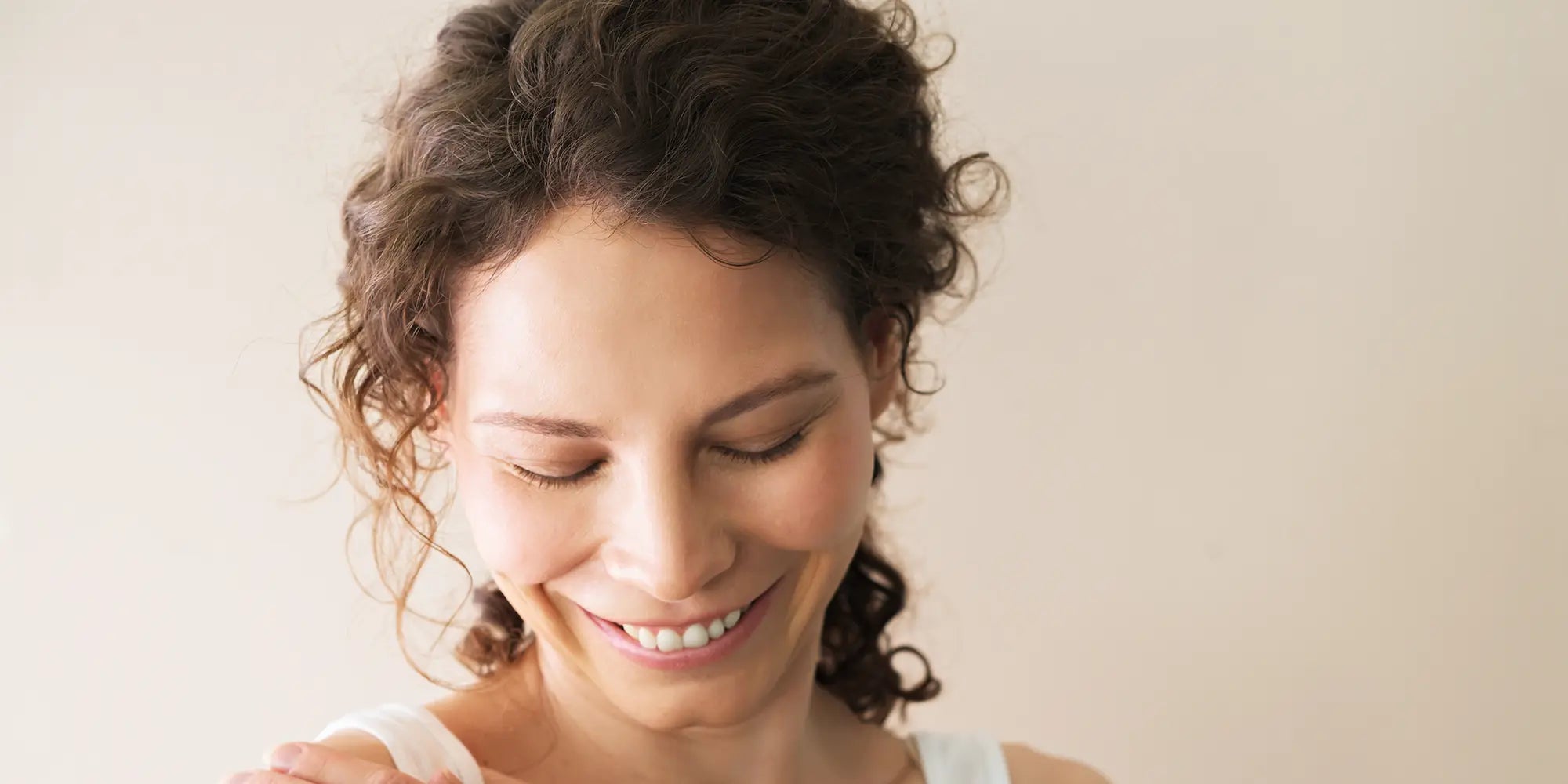 Woman with curly hair smiling against a plain background