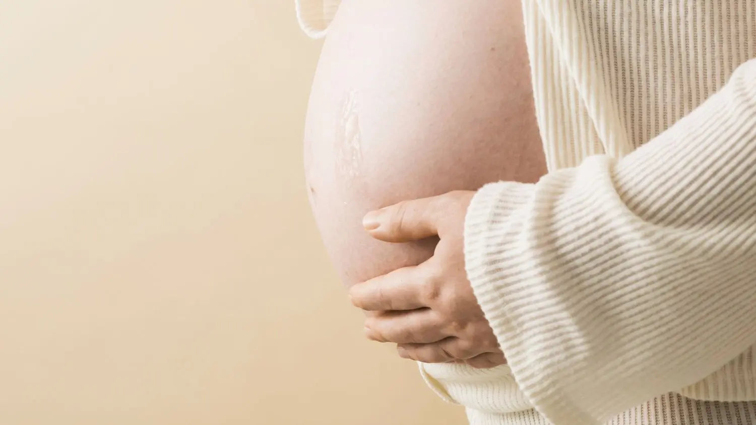 Pregnant belly with hands on a beige background