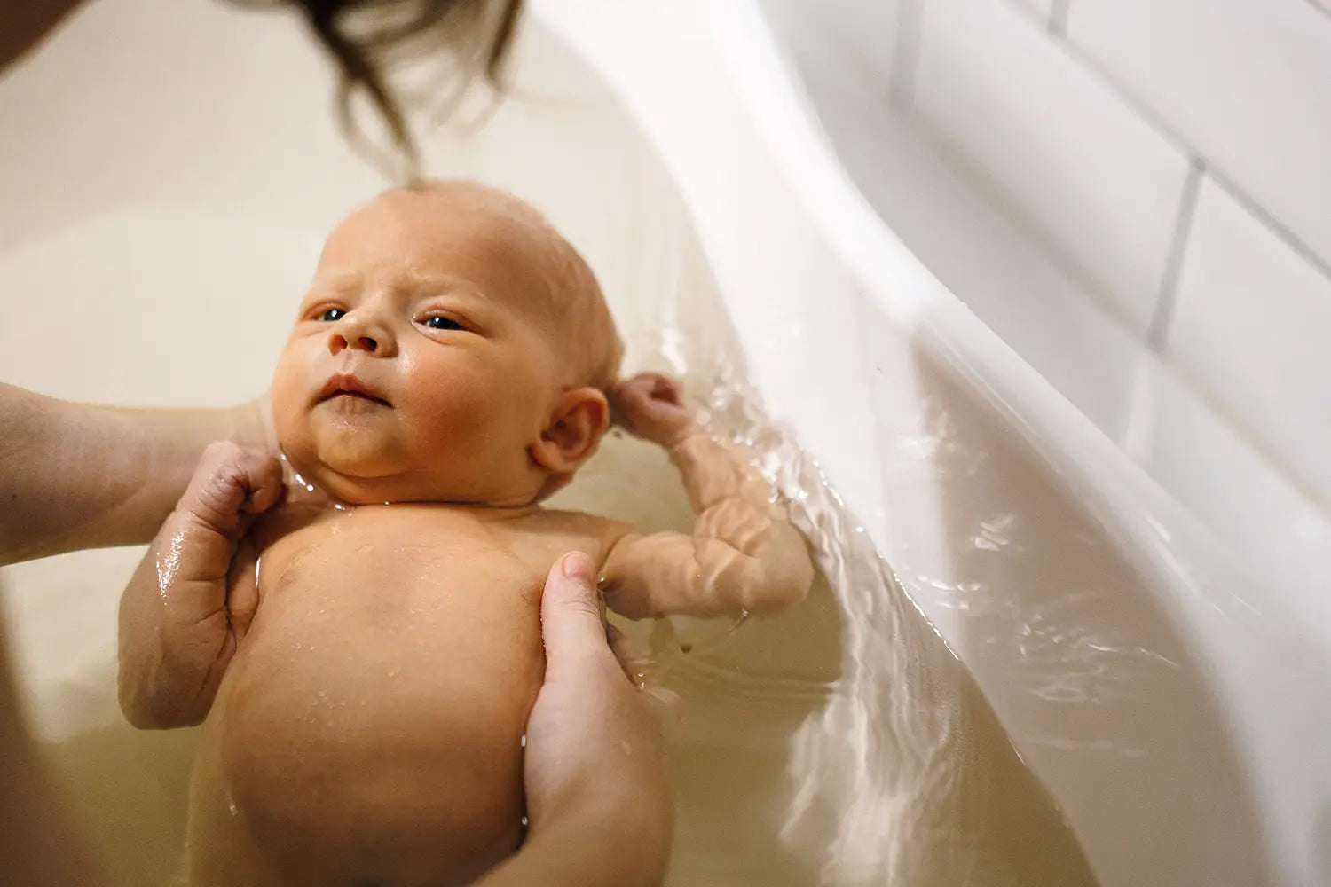 Baby being bathed by an adult in a bathtub.
