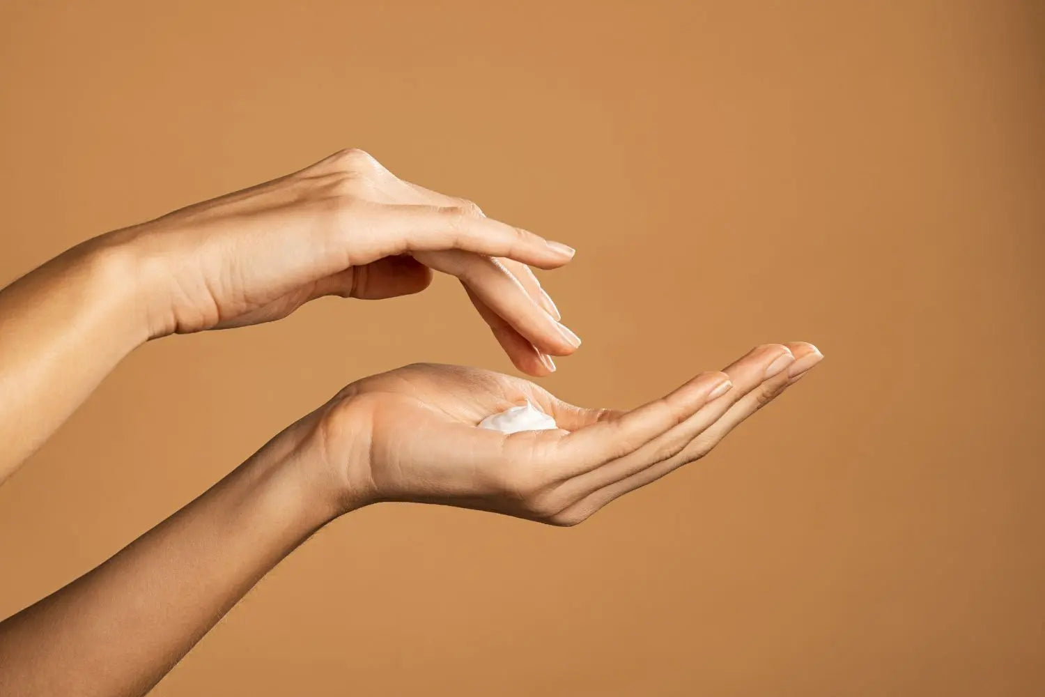 Two hands holding a small container of cream against a brown background